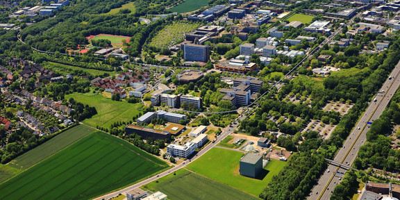 Zu sehen ist ein Luftbild von der TU Dortmund und FH Dortmund sowie umliegende Siedlungen, Straßen und Grünflächen.