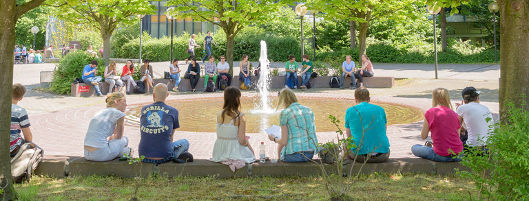 Studenten sitzen im Sommer am Brunnen des Martin-Schmeißer-Platzes